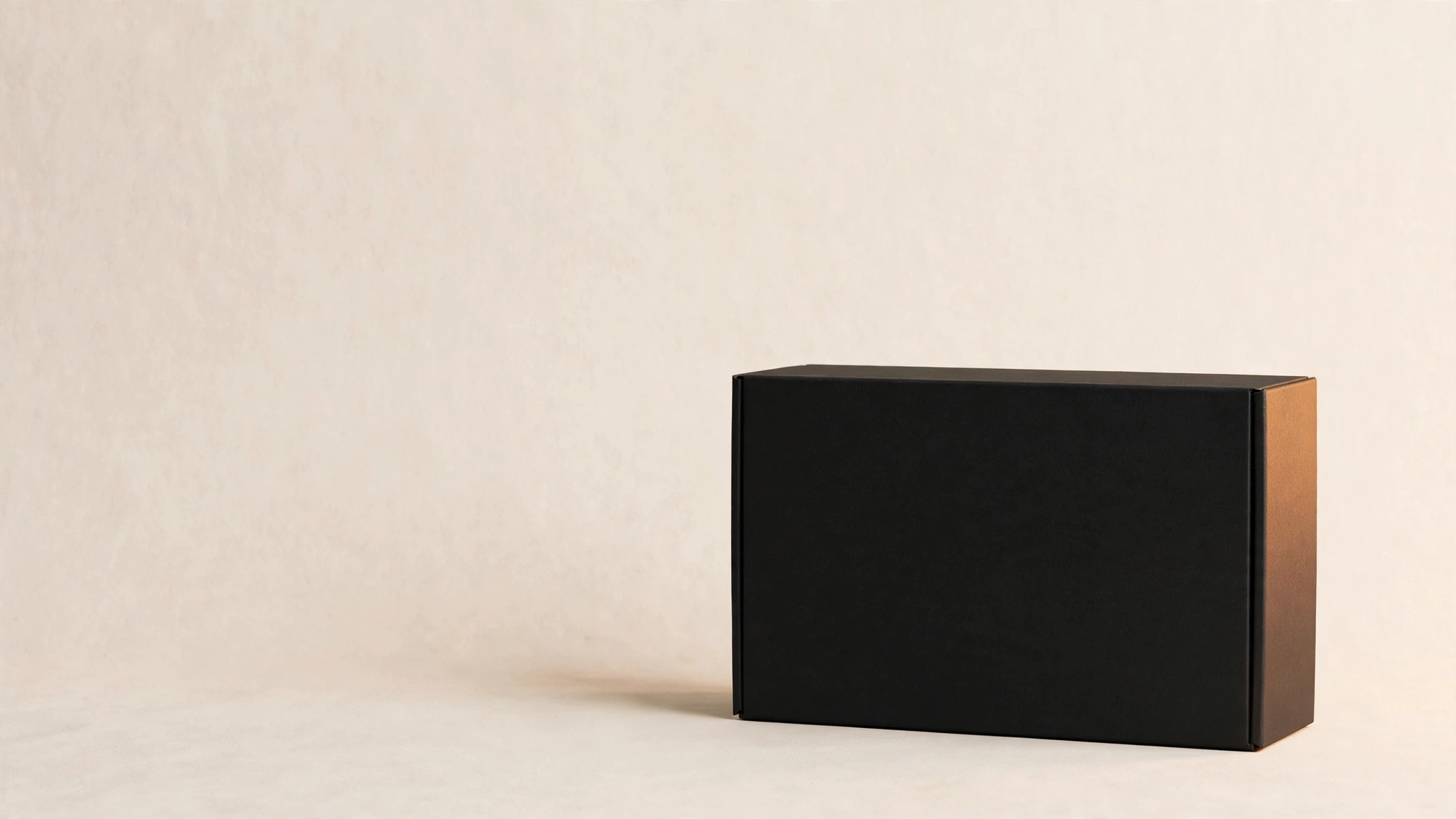 A sealed matte black box on a warm off-white backdrop, one edge catching light.