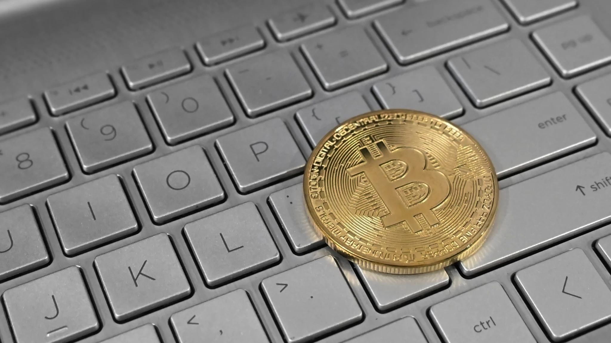 A physical Bitcoin token resting on a laptop keyboard.