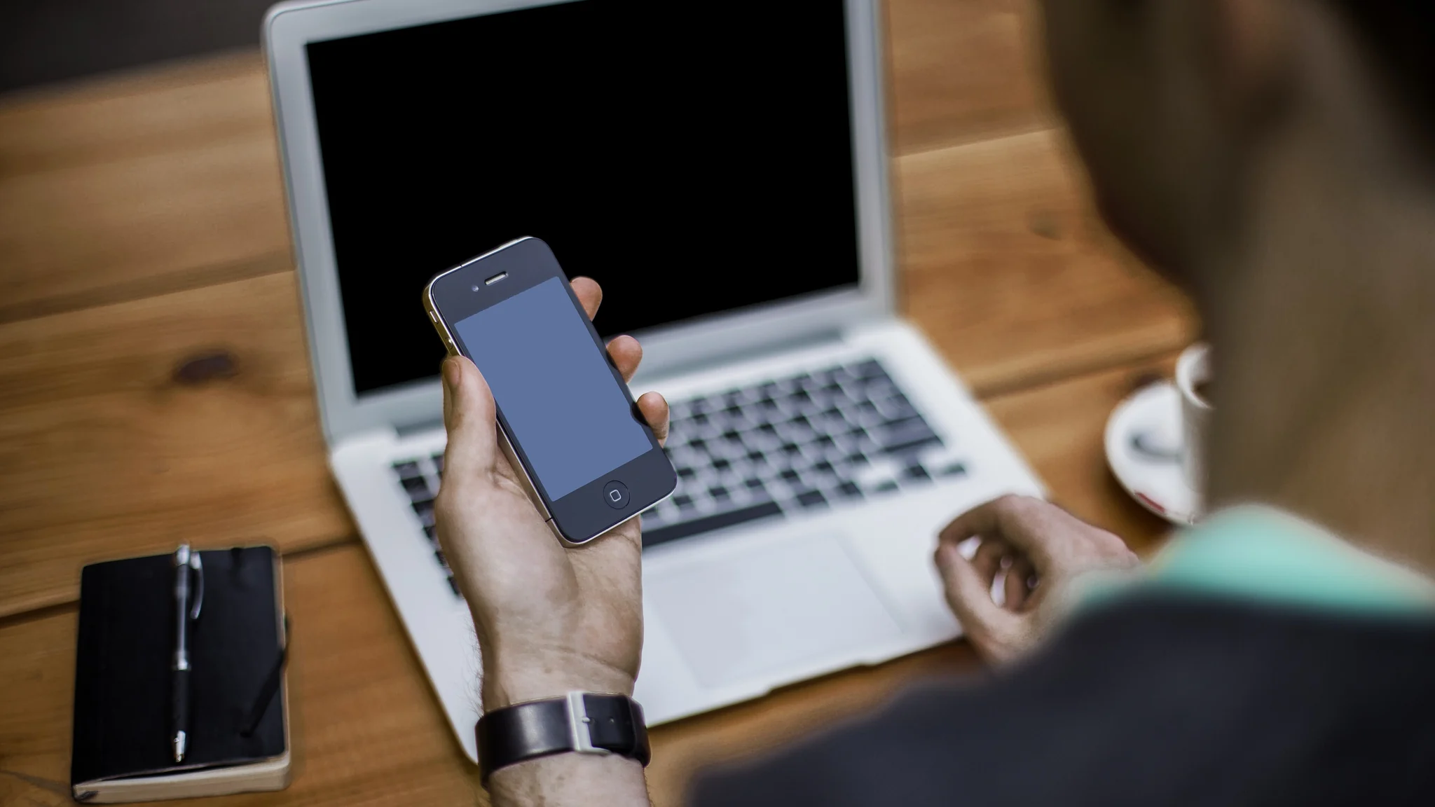 A man using a smartphone at a desk beside a laptop.